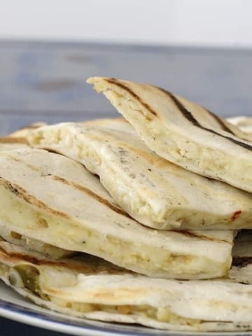 Quartered quesadillas on a plate with avocado on the side