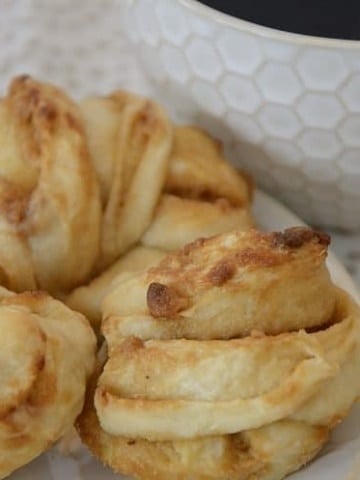 Golden cruffin knots of dough on a plate beside a cup of coffee.
