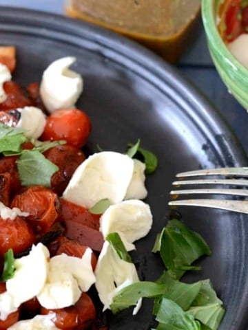 Salad with charred cherry tomatoes, charred peppers, mozzarella and basil on a platter.
